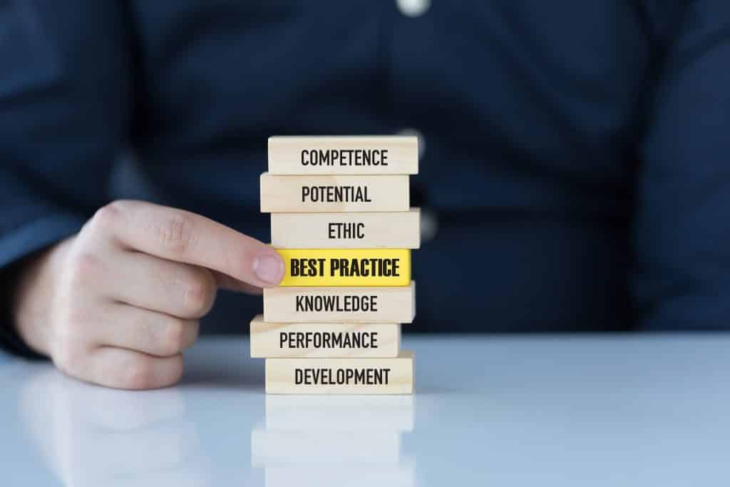 A hand arranges wooden blocks about best practices and professional standards.